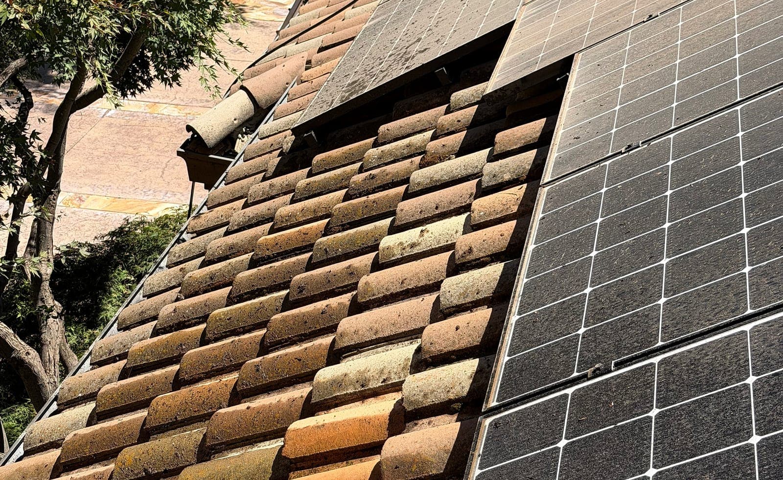 Clay barrel tiles meeting the edge of a solar array, with soiling and growth collected in the pans between the tile rolls