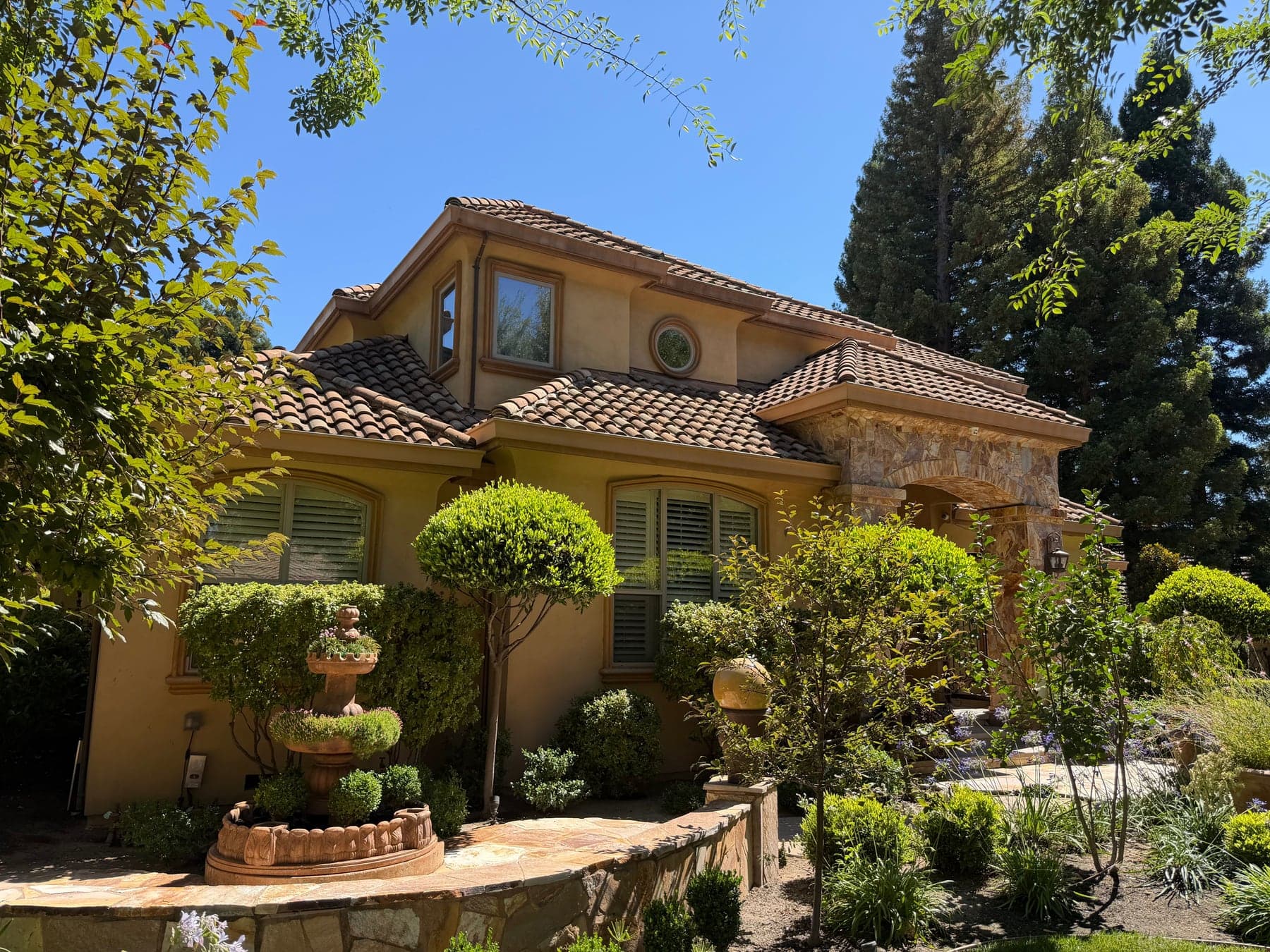 Two-story stucco home with a clay tile roof, arched windows and a stone entry, photographed during a house wash