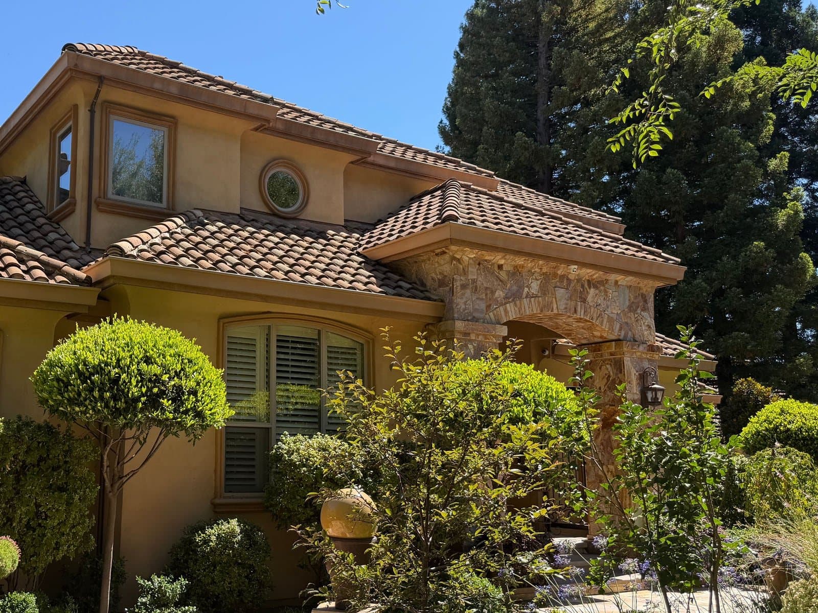 Upper-story arched and round windows set in a stucco wall under a clay tile eave