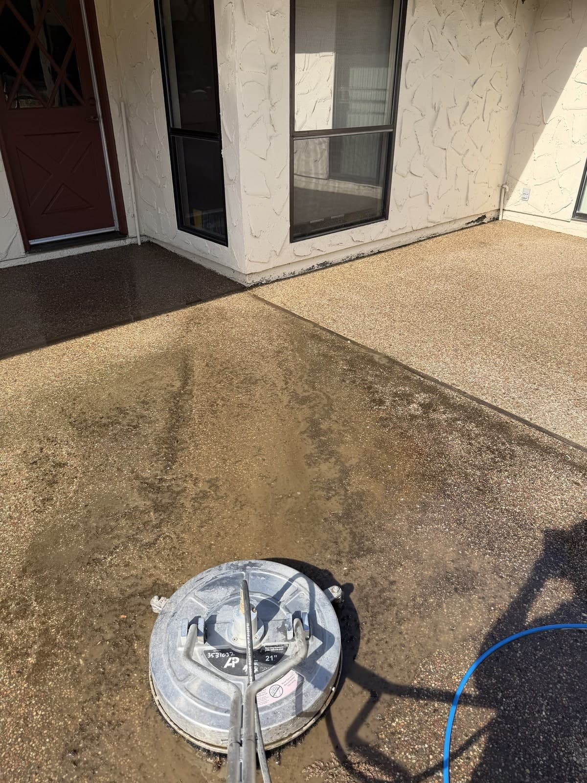 Aggregate patio mid-job: the surface cleaner has drawn a hard line between the cleaned concrete and the grime still ahead of it
